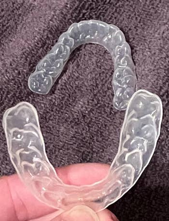 Clear dental aligners on a textured surface, likely used for teeth straightening