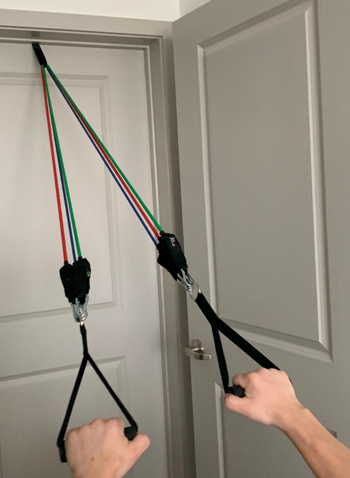 reviewer pulling bands from door frame for arm exercise
