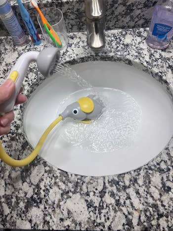 Elephant-shaped faucet attachment spraying water into a bathroom sink, shown for potential use in kid-friendly bath products