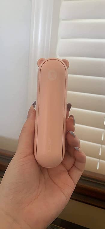 image of reviewer's manus  holding up   the pinkish  handheld fan