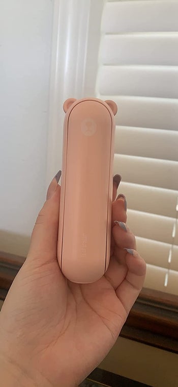 image of reviewer's hand holding up the pink handheld fan