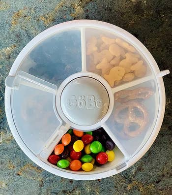 reviewer photo of the snack spinner filled with things like skittles, pretzels, goldfish, and dried fruit
