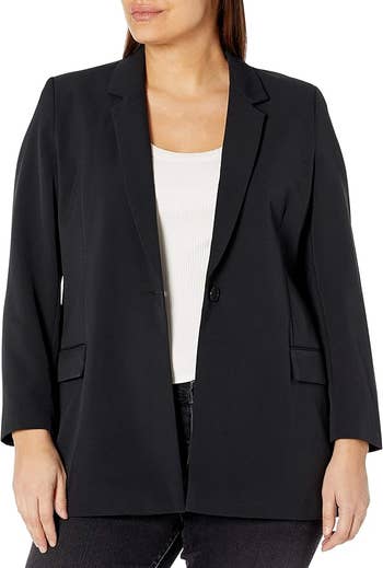 Orang yang mengenakan blazer satu tombol di atas atasan putih dan celana gelap. Wajah tidak terlihat. Tidak ada orang lain yang ada dalam gambar