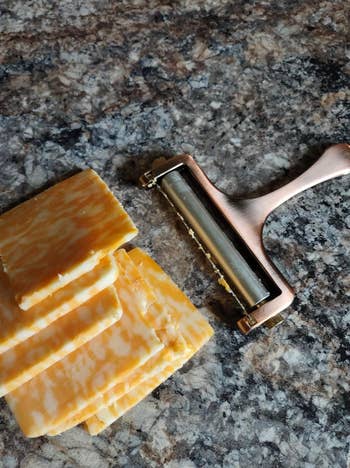 small handheld copper colored wire cutter next to a stack of cut cheese slices 