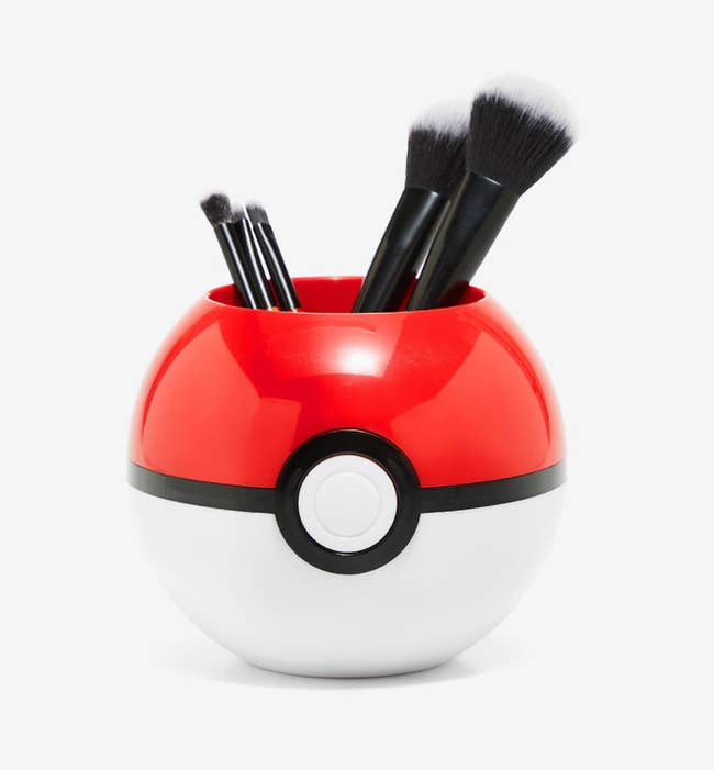 A pokeball-shaped container with makeup brushes in it 