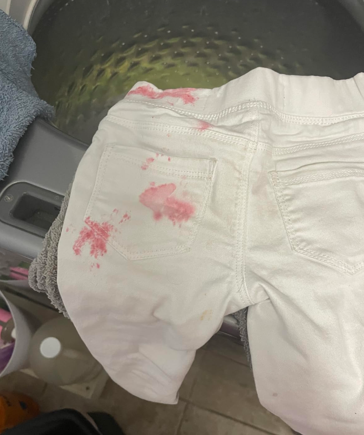 Stained white pants with a pink blotch on a washing machine