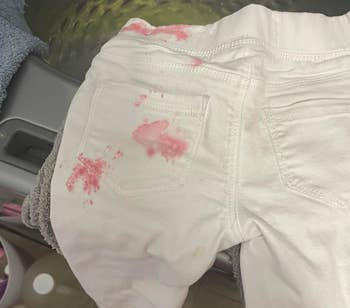 Stained white pants with a pink blotch on a washing machine