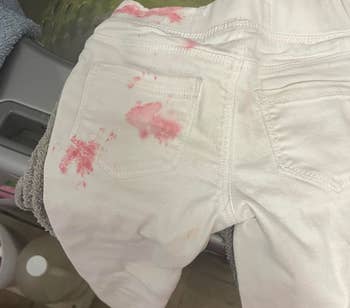 Stained white pants with a pink blotch on a washing machine