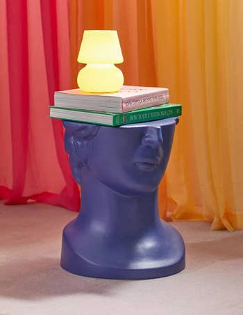 blue sculptural bust styled as a table with a stack of books and a small lamp on top