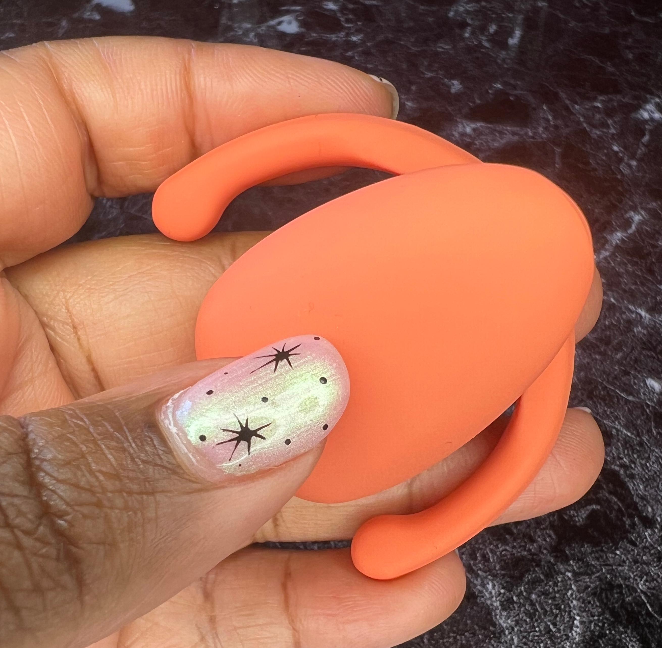Hand holding orange clitoral vibrator