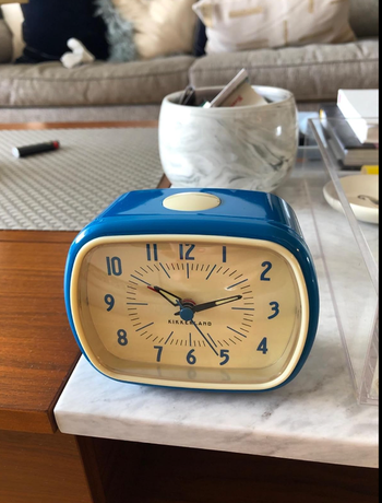 blue rectangular analog alarm clock with rounded edges perched on a table 