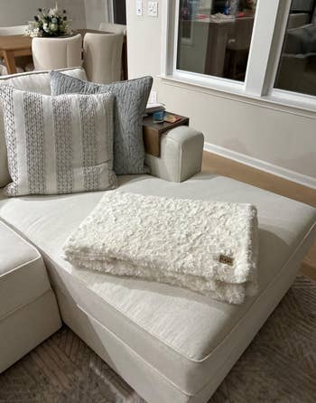 A cozy, textured throw blanket elegantly draped on a modern sectional sofa in a stylish, minimal living room setting