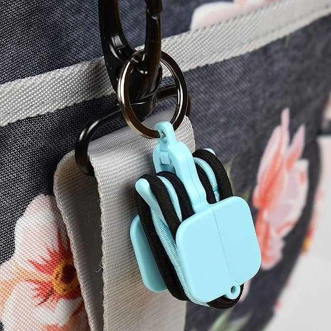 Portable blue plastic hair tie clip with carabiner attached to a floral-patterned fabric bag strap