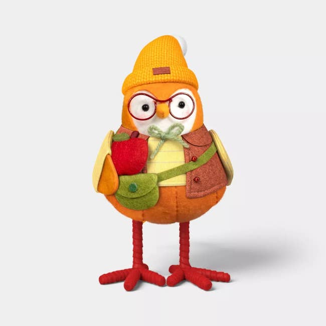 Plush owl artifact  with glasses, orangish  knit hat, and cozy autumn  vest, holding an apple