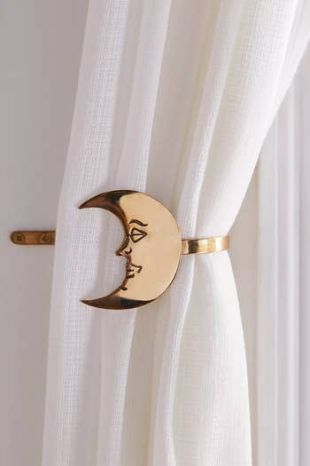 Gold moon-shaped curtain tieback holding white curtain. Elegant home decor accessory