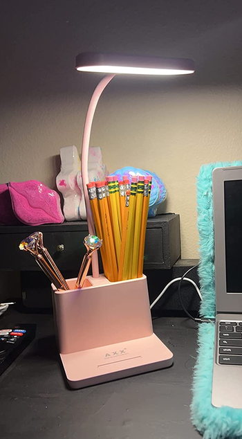 reviewer photo of a pink lamp with storage components full of pens and pencils on a desk