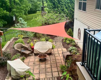 A backyard patio with a shaded seating area, covered furniture, and lush greenery surrounding a paved walkway