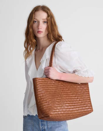 A pistillate   successful  a achromatic  blouse and jeans holds a woven tote bag, showcasing its size and texture for a buying  article