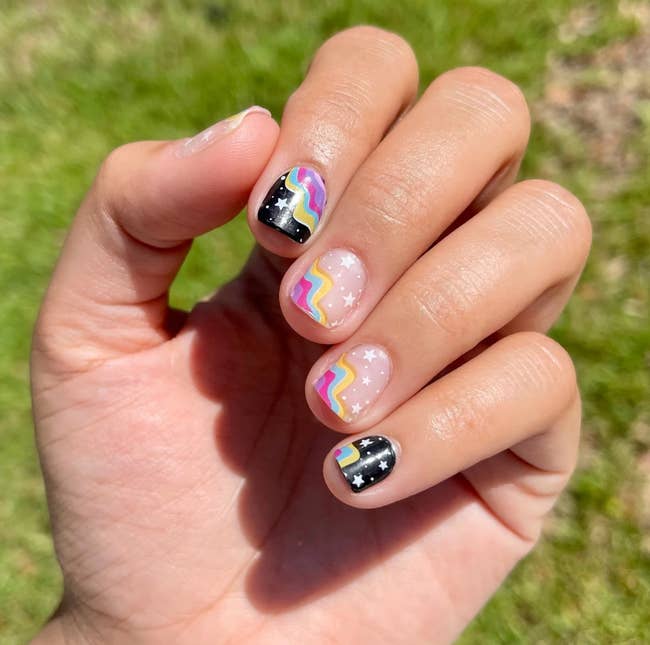 Model wearing rainbow nail wraps on top of stars manicure