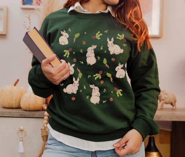 Model is wearing a dark green sweatshirt with seven small bunnies printing on it with turnips and carrots