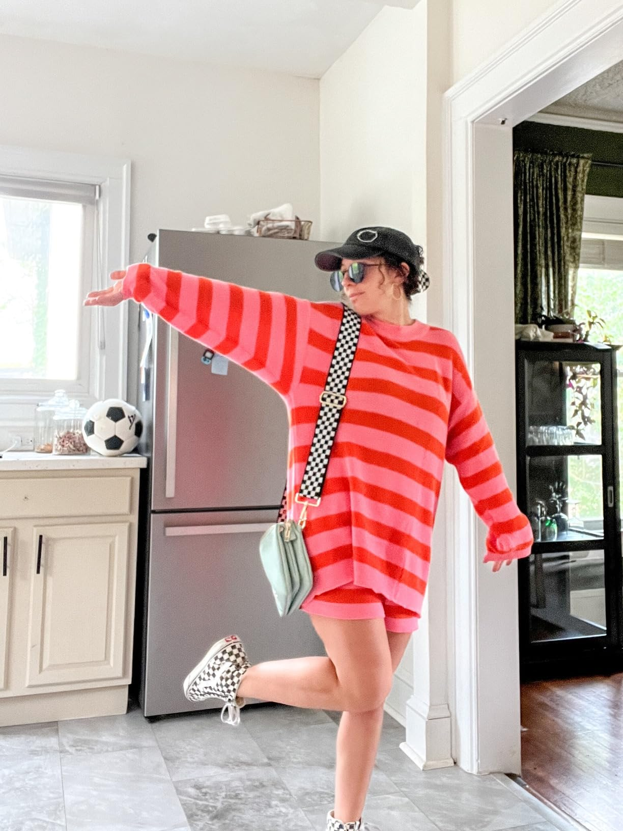 Person successful  a striped oversized sweater, checkered shoes, crossbody bag, and headdress  poses playfully successful  a kitchen