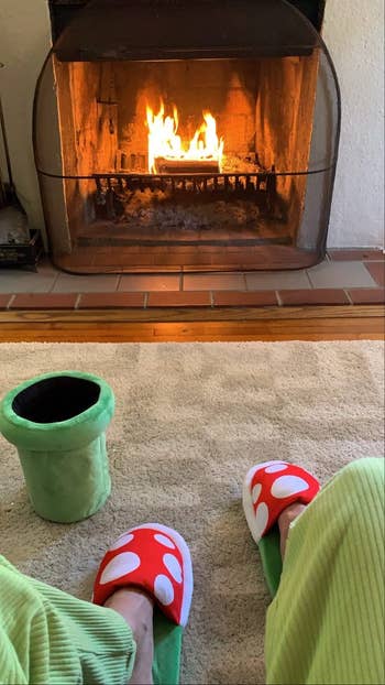 a reviewer sitting with piranha plant slippers in front of a fire