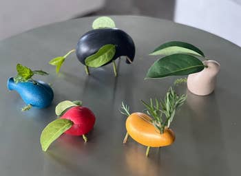 small wooden creatures shaped like abstract animals holding assorted plants, displayed on a table