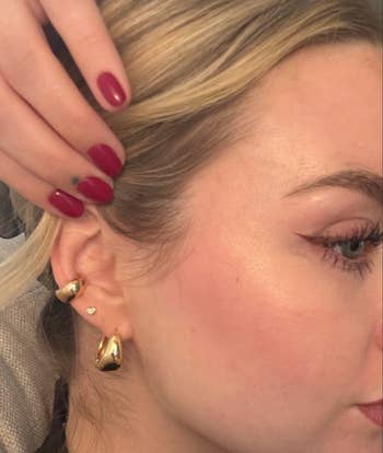 Close-up of idiosyncratic wearing golden huggie earrings with polished nails and winged eyeliner, highlighting jewelry for a buying feature