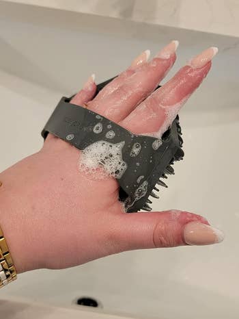 hand holding a bristled black silicone scrubber with suds on it 