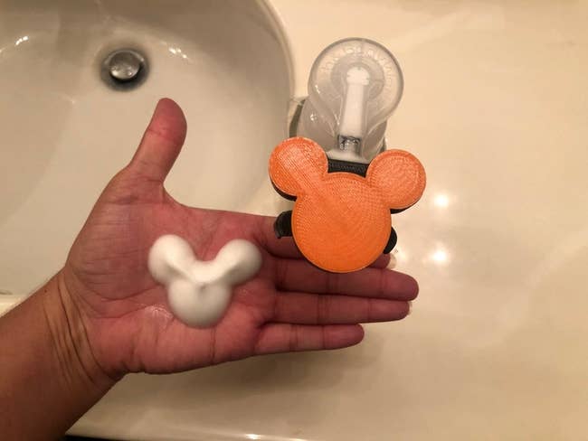 hand using the orange pump to pump out mickey face and ears-shaped foam soap