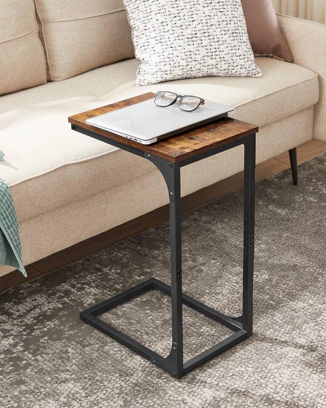 Slim C-shaped end table next to a couch with a laptop, glasses, and notepad on top