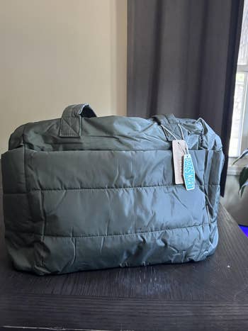 Quilted handbag with a short handle and a visible tag on a table, suitable for casual outings