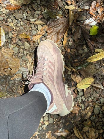Person wearing hiking sneaker, standing on a leafy, gravel path