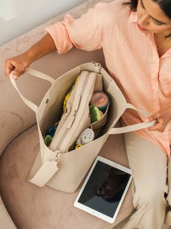 a model opening the interior of a full beige tote bag