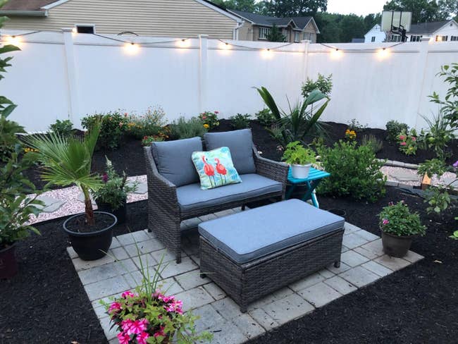Patio furniture set with cushions and a side table, in a garden with hanging lights