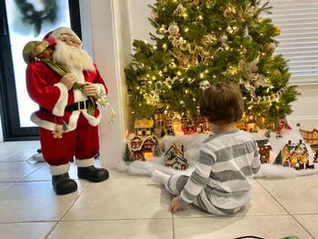 Child successful  striped pajamas sits by a Christmas histrion   and a Santa Claus figure, looking astatine  a festive colony   setup