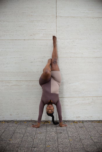 model wearing the two-tone long-sleeved body suit while doing a headstand against a wall