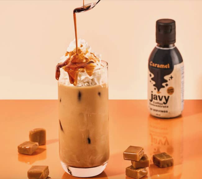 an iced coffee with syrup being poured on top with caramel Javy bottle in the background