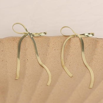 Two gold bow earrings displayed made of snake chain
