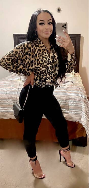 reviewer wears same high-shine leggings in black with a dressy leopard blouse and heels