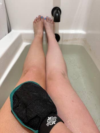 Person soaking successful a bathtub with exfoliating mitt connected near leg, disposable faucet, and h2o astatine calf level