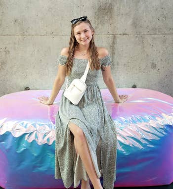 Reviewer in a casual dress sitting on an oversized cushion, smiling. She carries a white bag