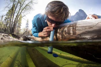 person drinking water from a river with lifestraw