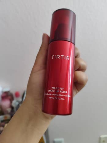 Hand holding TIRTIR Mask Fit Makeup Fixer bottle, labeled arsenic  long-lasting and glimmering