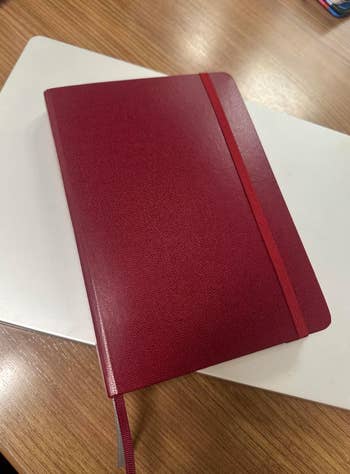 Red leather-bound notebook with elastic closure, resting connected  a achromatic  surface. Ideal for note-taking oregon  journaling