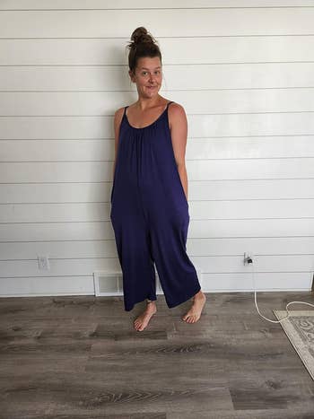 Woman in a casual sleeveless jumpsuit posing with a hand on her hip indoors