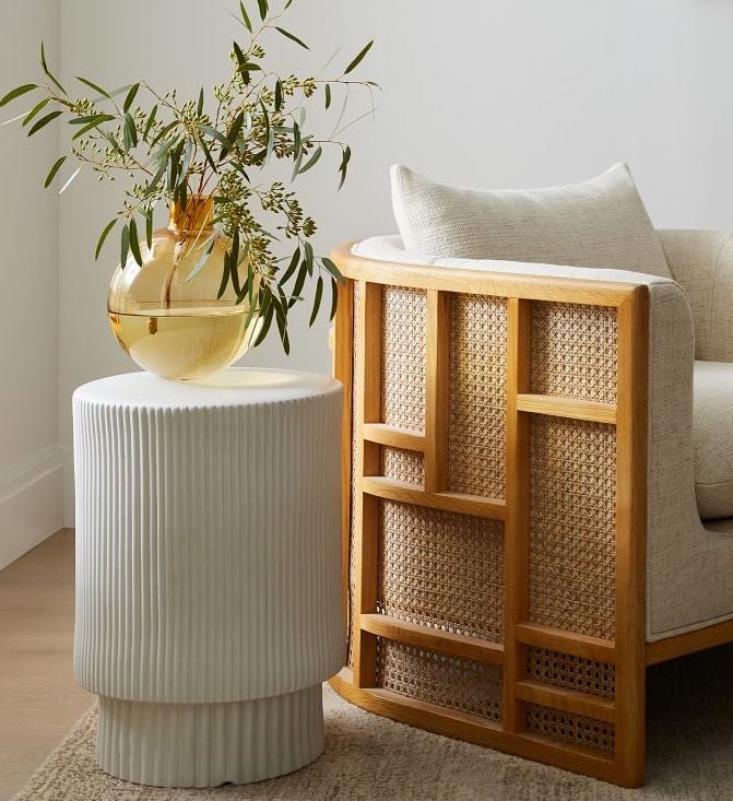 the white side table holding a yellow vase next to a rattan arm chair