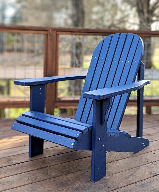 Cobalt blue Adirondack wooden chair outside on a brown wooden deck 