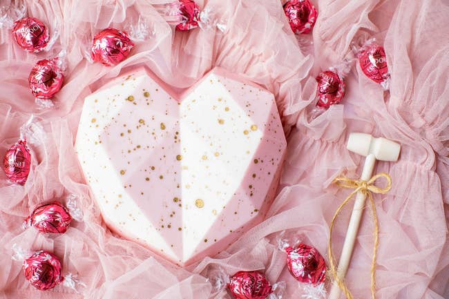the pink chocolate heart with gold specs with truffles in pink wrapper around it and a mallet