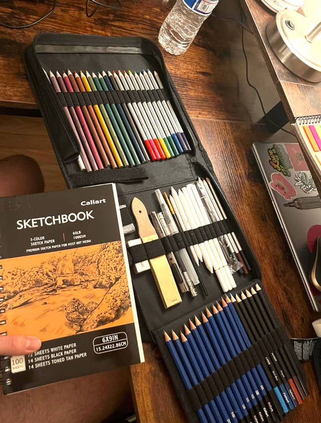 Art supplies connected  a woody  desk, including a acceptable   of colored pencils, graphite pencils, blending tools, and a sketchbook labeled 